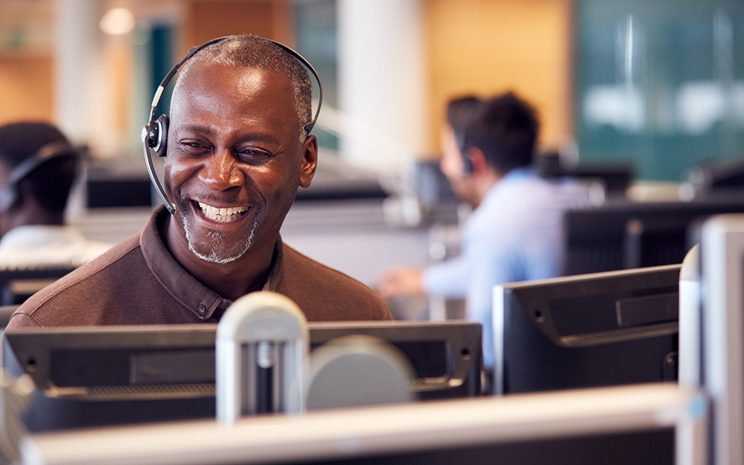 Mature Businessman Wearing Telephone Headset Talking To Caller In Customer Services Department
