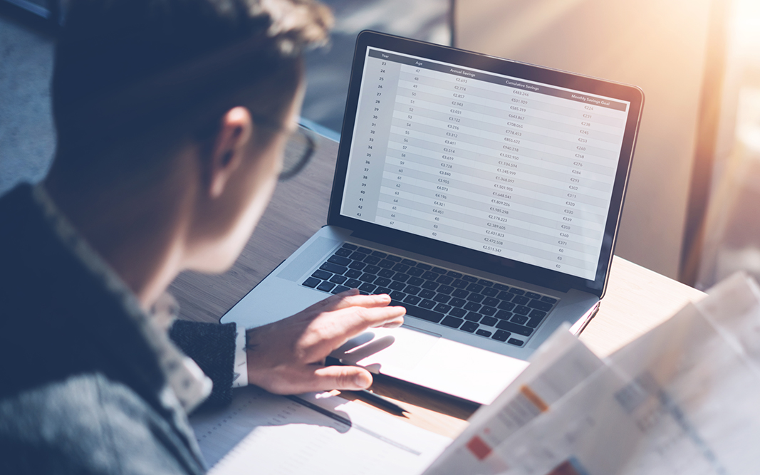 Closeup view of banking finance analyst in eyeglasses working at sunny office on laptop while sitting at wooden table.Businessman analyze stock report on notebook screen.Blurred background,horizontal.